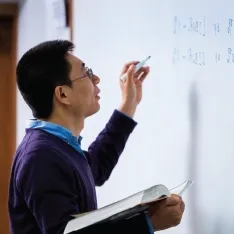 A professor writing on a whiteboard in a math course.